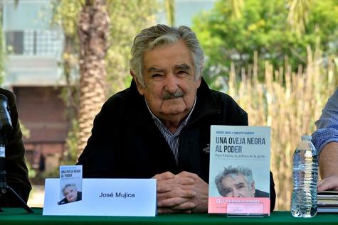 Former Uruguay president José Mujica sits at a desk with his hands together. His book sits infront of him standing up at a talk about the new publication.