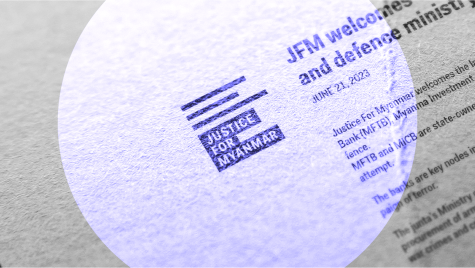 A spotlight shines over a printed paper with the logo for Justice For Myanmar in the centre.