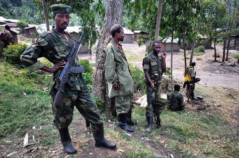 Five Congolese soldiers for the M23 Rebels stand and sit in the trees at the sit of the road.