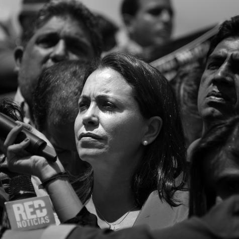 Black and white image of Venezuelan politician María Corina Machado. She looks seriously off to one side standing in a crowd of people.