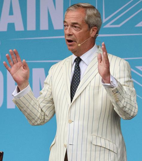 Nigel Farage wearing a white pinstripe suit addresses a Reform UK rally at Trago Mills, Devon