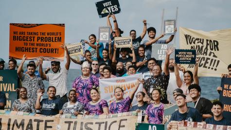 A group of Pacific Island protesters pose for a photo whilst demonstrating action for climate change. They hold poster which say 'Endore the AO' and 'Vote yes for climate justice'