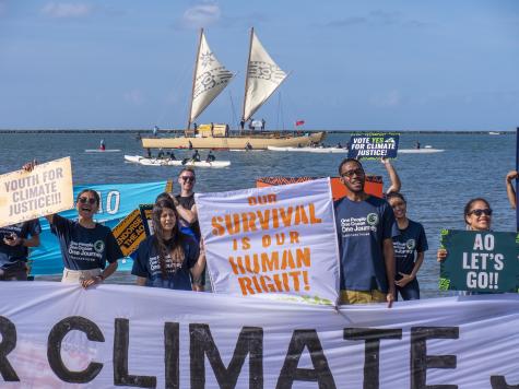 Protesters stand at the shoreline campaigning for climate justice. They hold a large white sign that says 'Survival is our human right'
