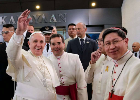 Pope Francis arrives in the Philippines and smiles and waves at the camera surrounded by members of the Papal Delegation