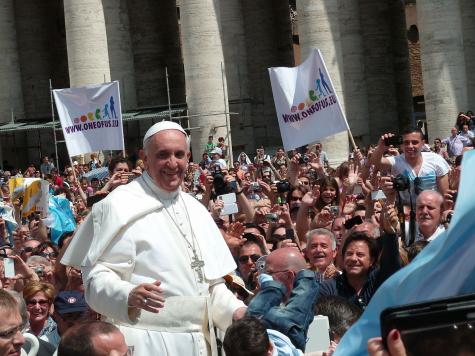 The Pope wears all white robes and is in the centre of a large crowd at St. Peter's Square
