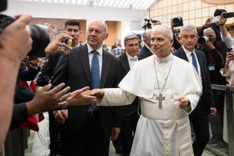 Pope Leo XIV - Audience For Journalists. Dressed in all white Pope Leo walks through the crowd and shakes the hand of an audience member.