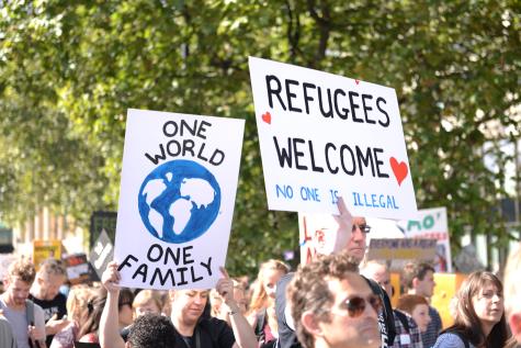 Pro-migration protest where demonstraters are holding signs which say 'One world' and 'Refugees Welcome'.