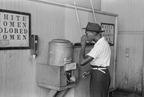 A Black man drinking at "Colored" water cooler in streetcar terminal, Oklahoma City.