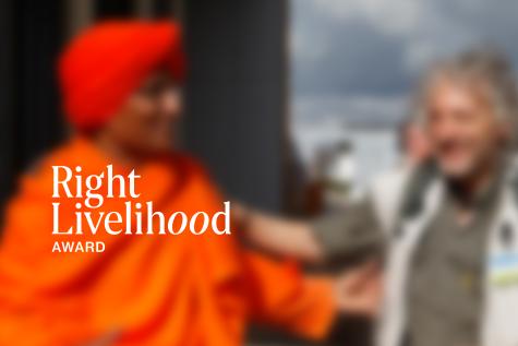 Right Livelihood image from the press kit. Two people are blurred in the background with RLA logo in focus up front.