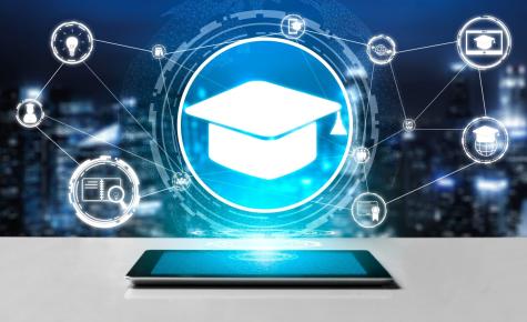 A tablet sits on a table. In the background there is a graduation cap and many other symbols representing learning.