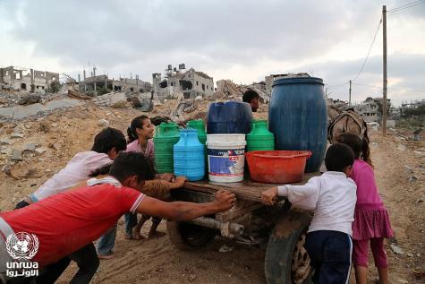 Children help to push a wooden cart in Gaza carrying buckets of water.