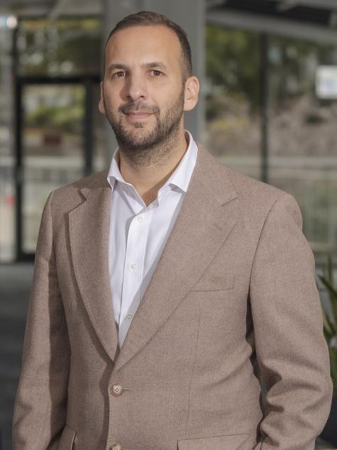 Leader of the Green Party Zack Polanski poses for a portrait wearing a beige suit and white shirt. 
