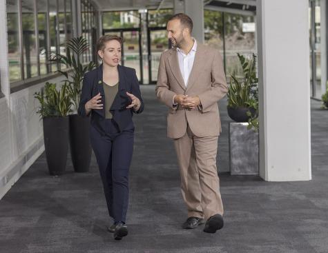 Green Party members Zack Polanski and Carla Denyer walk down a hallway in conversation. 