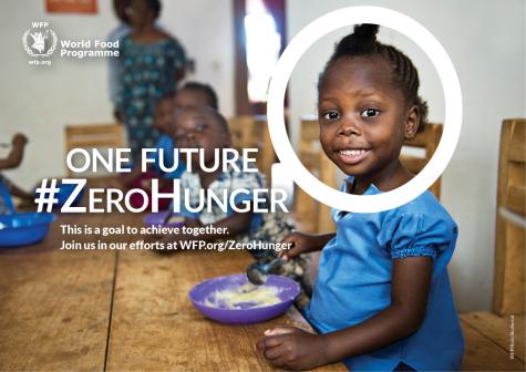 The World Food Programme's social media image for World Food Day in 2015. A young African child sits smiling at a wooden table with a bowl of food infront of her.