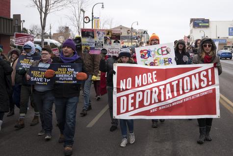 A diverse group of protesters march down a street, holding signs advocating against deportations.