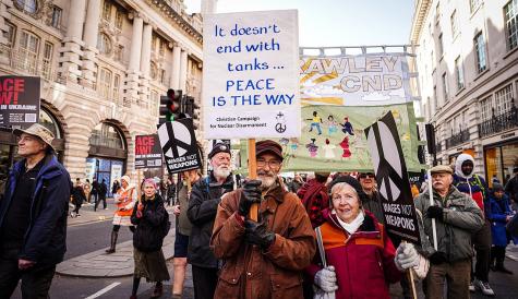 A diverse group of protesters holding signs, advocating for peace during a demonstration on a city street.