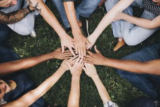 Many different peoples hands join in the centre of a circle