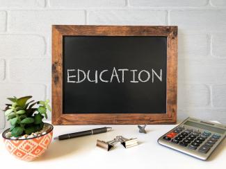 Black chalkboard displaying the words 'education' with a calculator, pens, and other smll objects placed infront