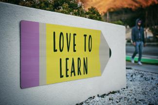 A big white concrete sign displays a graphic of a large yellow pencil with the words 'love to learn' on it