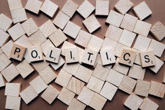 Beige coloured wooden Scrabble letters spell out the word politics on top of many other blank square pieces