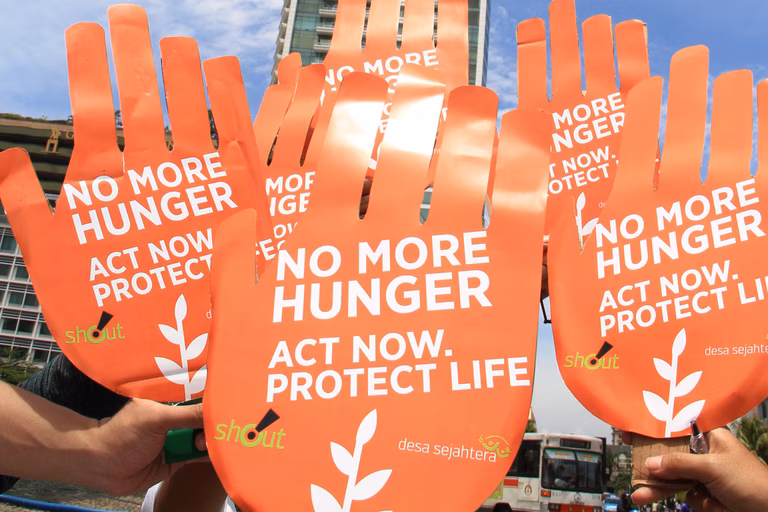 6 giant orange hands are held in the air display the words 'No more hunger. Act now'