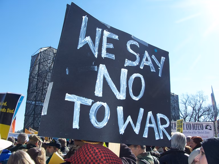 At an anti-war demonstration there is a large black sign that says 'We Say No To War'.