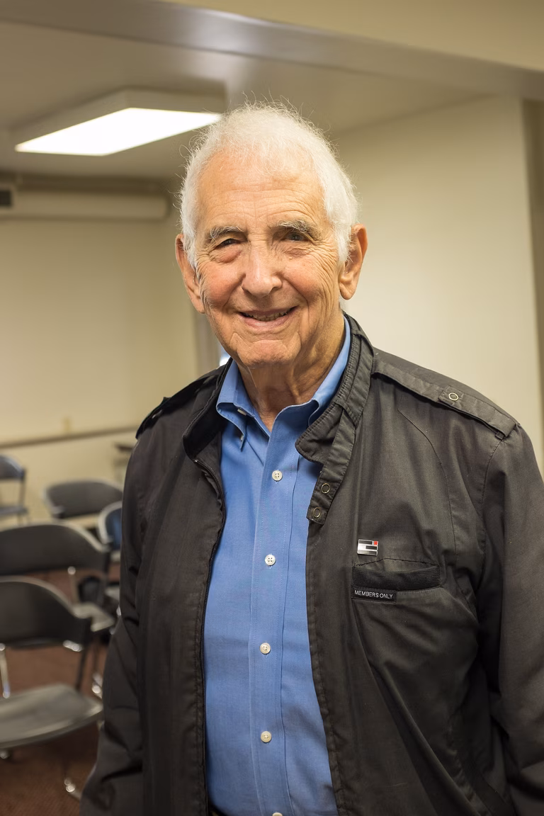 Image of Daniel Ellsberg U.S. whistle-blower. A senior white male smiles warmly into the camera wearing a white shirt and black&nbsp;jacket. 