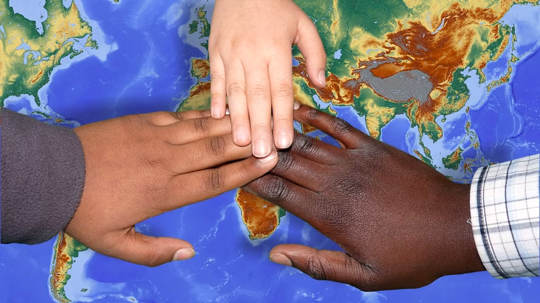 Three hands of different skin colour touch in the centre of a map of the world
