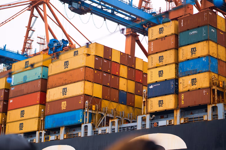 Different coloured shipping containers sit stacked ontop of each other on a freight ship