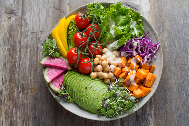 A huge bowl of colourful vegatables sits on a grey table. 