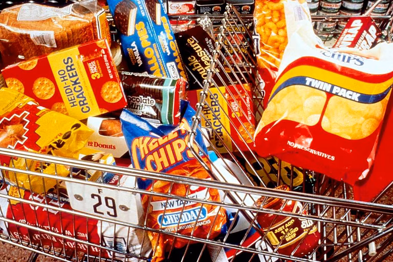 A shopping cart in a supermarket is filled to the brim with chocolate, crisps, sweets, and biscuits