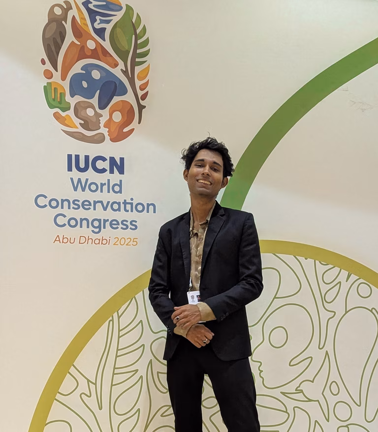 Author Tanuj Samaddar posing in front of the main banner of the World Conservation Congress 2025 in Abu Dhabi