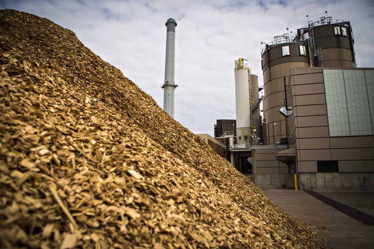 Image of a biomass boiler with two large chimneys and a large pile of wood chips in the foreground