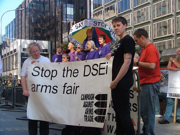 CAAT protesters hold a large white banner which says 'Stop the DSEi arms fair'