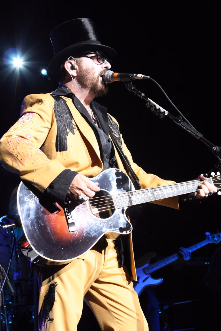 Musician Dave Stewart performs on stage wearing a yellow suit and a black top hat.