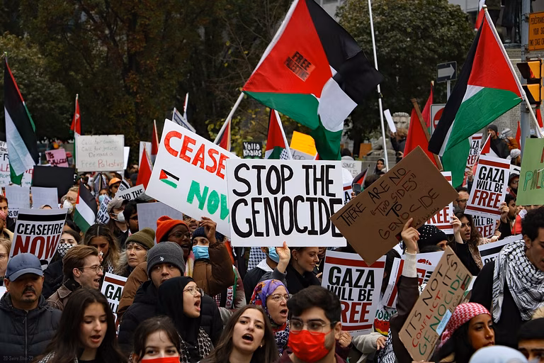 Pro-Palestine protesters line the streets of Toronto holding signs which say 'Stop the genocide'.
