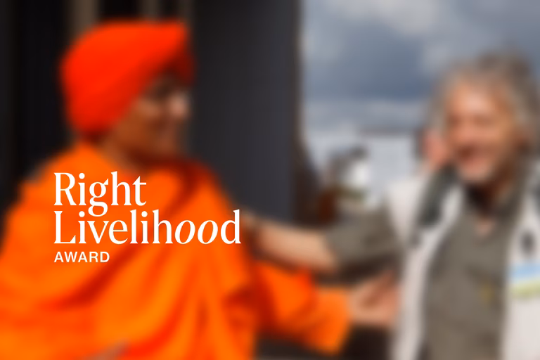 Right Livelihood image from the press kit. Two people are blurred in the background with RLA logo in focus up front.