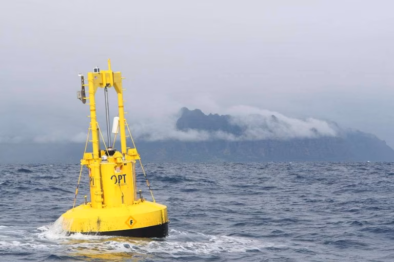 A yellow wave energy buoy floats off the east coast of Hawaii. There are cloudy mountains in the background