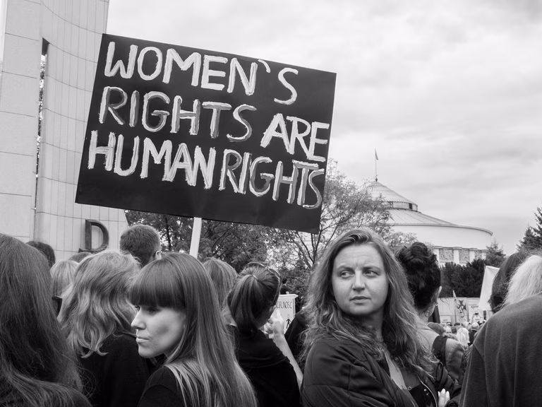 Black and white image of women protesting for women's rights. There is a large black sign saying 'Women's Rights are Human Rights'