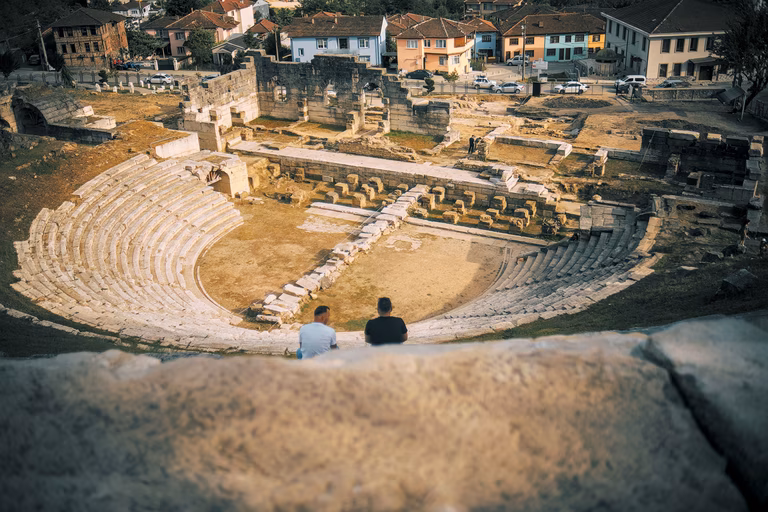 Aerial view of the ruins of a Roman amphitheatre as two people are overlooking from above