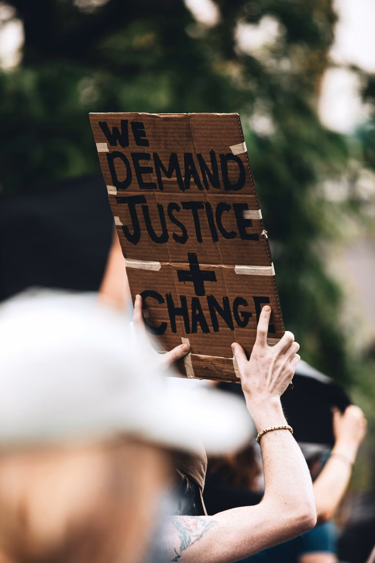At a demonstration a person holds a sign that says we demand justice and change.