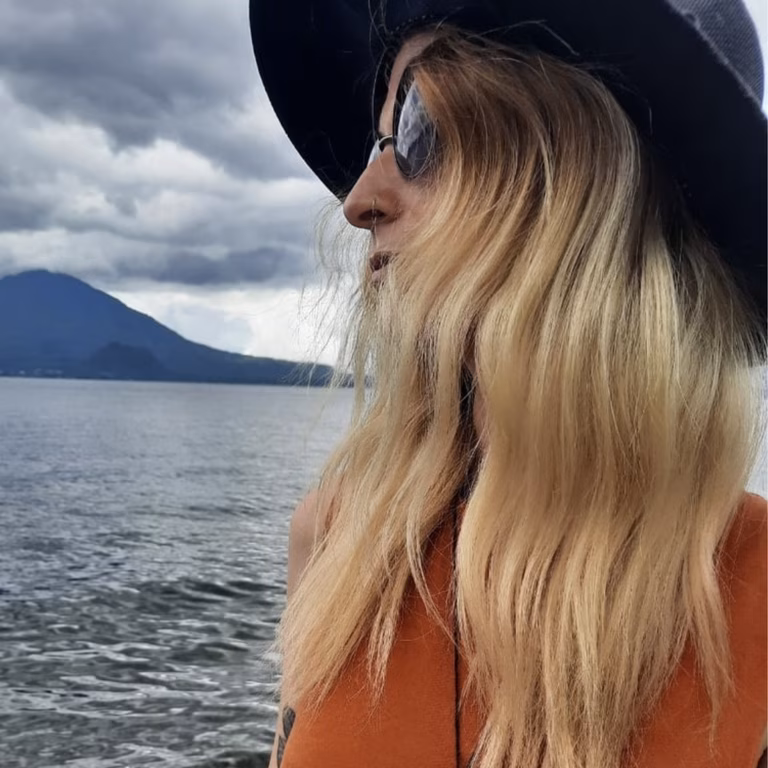 Image of a woman standing on the beach infront of a volcano. She is wearing sunglasses and is turned away from the camera.